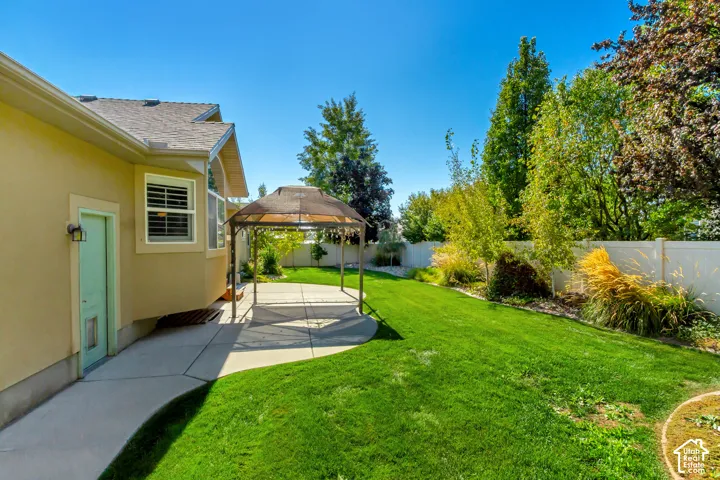 Expansive backyard oasis featuring a manicured lawn, mature landscaping with mixed plantings and evergreens, concrete patio, and wooden pergola structure