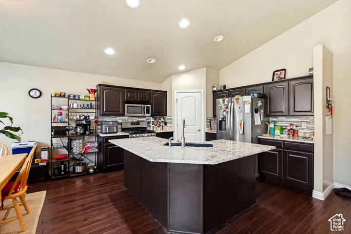 Kitchen featuring a central island with a sink, dark wood-finish cabinetry, stainless steel appliances, and wood-finish flooring