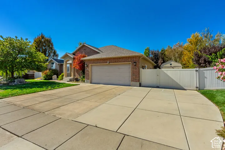 Brick exterior with an attached garage, featuring a concrete driveway, a white privacy fence, and mature landscaping