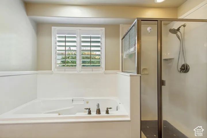 Built-in soaking tub with deck-mounted fixtures, separate glass-enclosed shower, and window with interior plantation shutters
