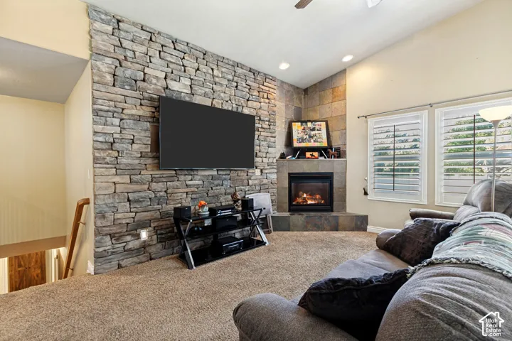 Stone-accented wall with integrated fireplace, vaulted ceiling, recessed lighting, and wood-slat window treatments