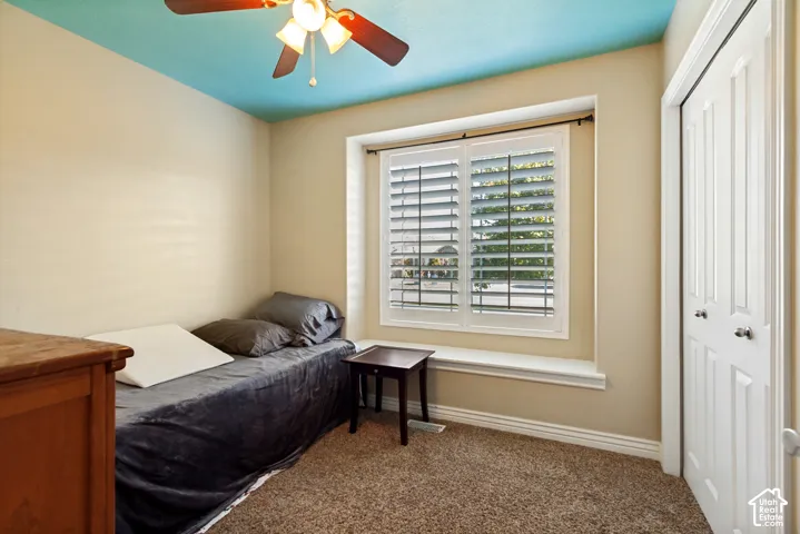 Window with white plantation shutters, textured carpeting, ceiling fan with integrated lighting, and bi-fold closet doors