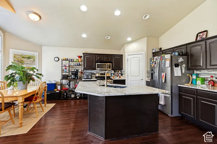 Kitchen featuring wood-finish flooring, dark wood cabinetry, stainless steel appliances, a center island with a sink, and recessed lighting