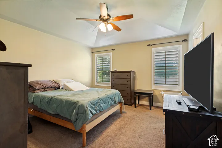 Tray ceiling with a ceiling fan, two windows with plantation shutters, and carpeted flooring