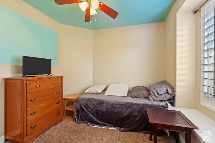 Carpeted room featuring a ceiling fan, window with shutters, and a built-in window seat