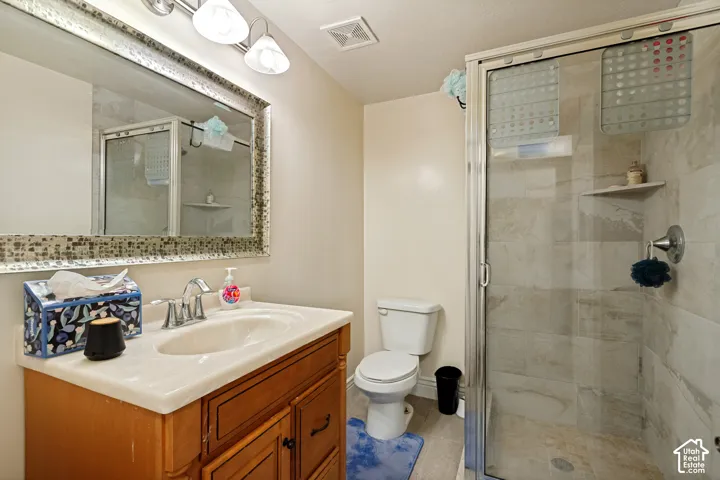 Wood-finish vanity with an integrated sink and chrome faucet, mosaic-framed mirror, and a glass-enclosed shower with tiled walls and a built-in corner shelf