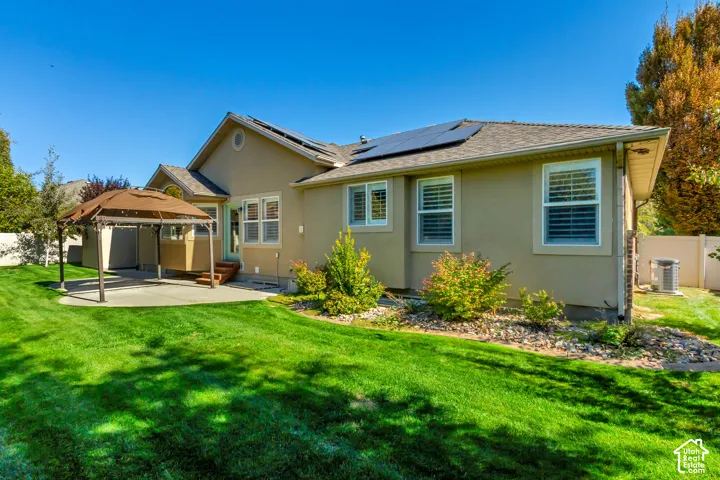 Expansive green lawn, stucco exterior, multiple windows with shutters, solar panels, and a concrete patio