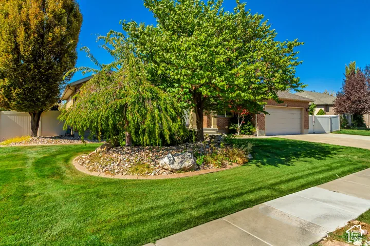 Manicured lawn, mature trees, landscaped planting beds, concrete driveway, and brick exterior