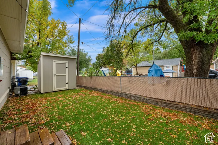 Spacious backyard oasis featuring a level lawn, mature shade trees, and a detached storage shed with white-trimmed entrance