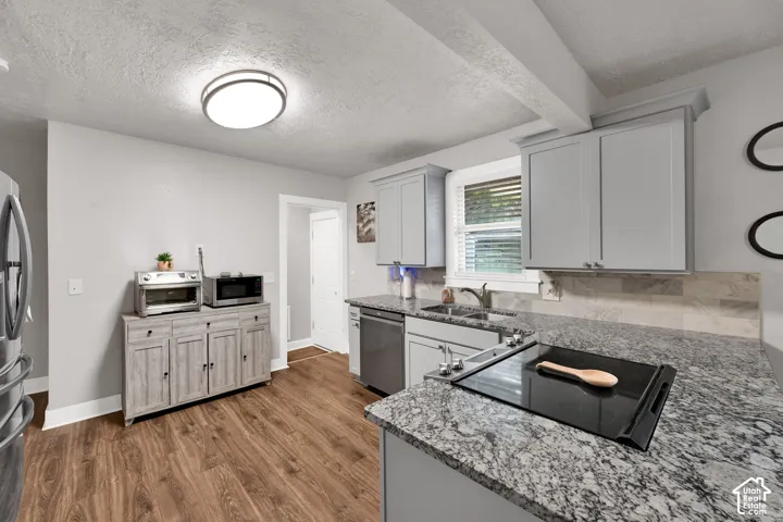 Kitchen featuring gray cabinetry, stone-finish countertops, wood-finish flooring, integrated electric cooktop, and stainless steel dishwasher