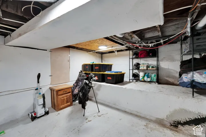 Unfinished storage area featuring painted masonry walls, concrete flooring, exposed ceiling joists, and integrated structural shelving ledge