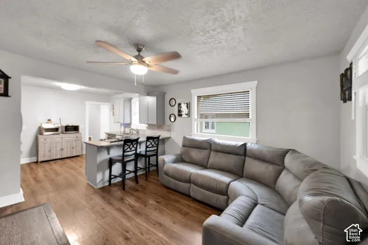 Wood-finish flooring, ceiling fan with integrated lighting, kitchen peninsula with breakfast bar, and neutral wall tones