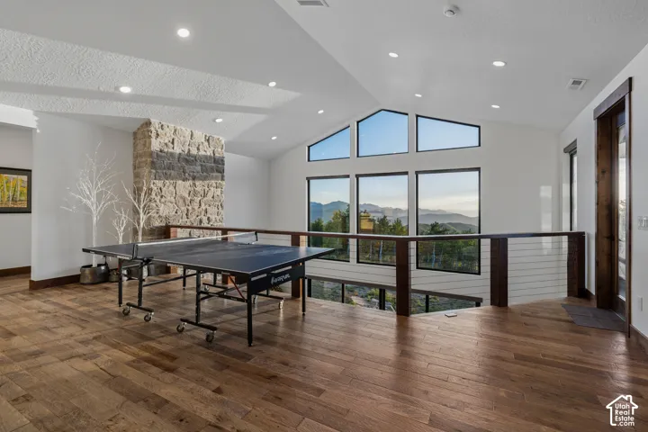 Vaulted ceiling with recessed lighting, wood-finish flooring, stone-clad fireplace, and large picture windows