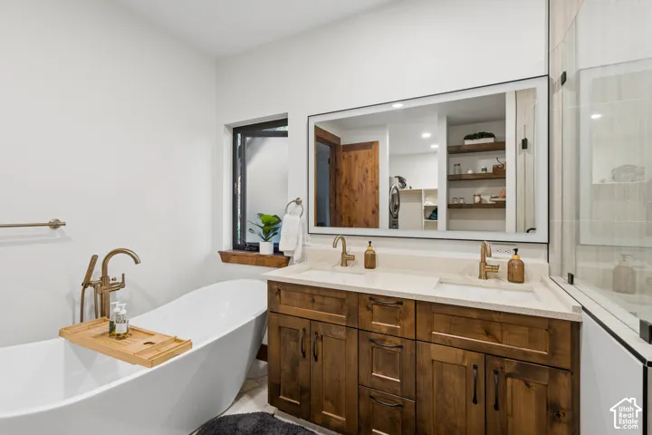 Freestanding soaking tub with floor-mounted faucet, dual vanity with undermount sinks and light-toned countertops, and a large wall-mounted mirror
