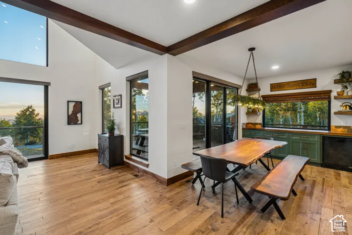 Vaulted ceiling with exposed wood beams, wood-finish flooring, full-height windows, green lower cabinetry, and open shelving