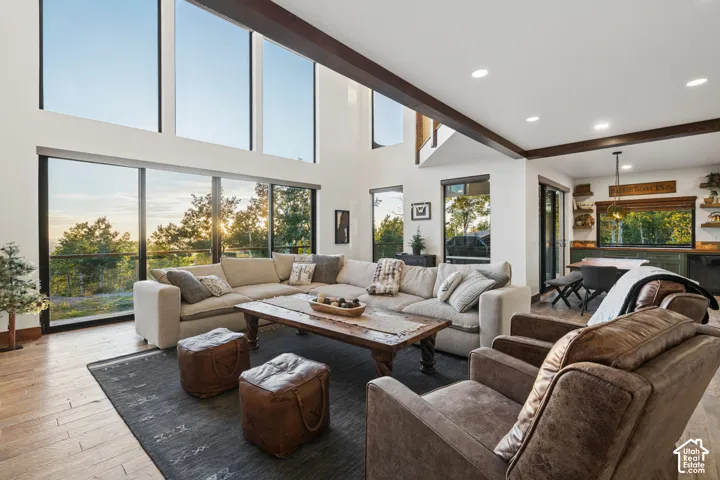 Vaulted ceiling with exposed wood beams, expansive floor-to-ceiling windows, recessed lighting, wood-finish flooring, and built-in shelving with integrated lighting