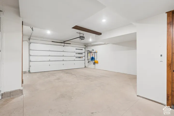 Concrete flooring, white overhead garage door, recessed lighting, exposed ceiling beam, wood-finish door frame
