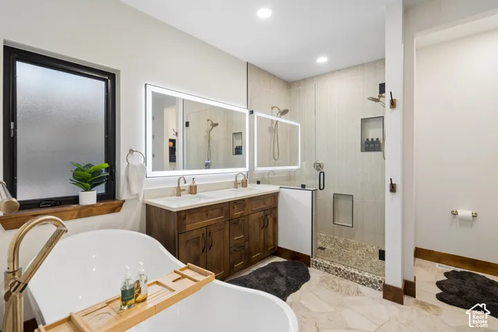 Spacious bathroom featuring a freestanding soaking tub with a floor-mounted brass faucet, a double vanity with a stone countertop, an illuminated mirror, and a glass-enclosed shower with a pebble floor