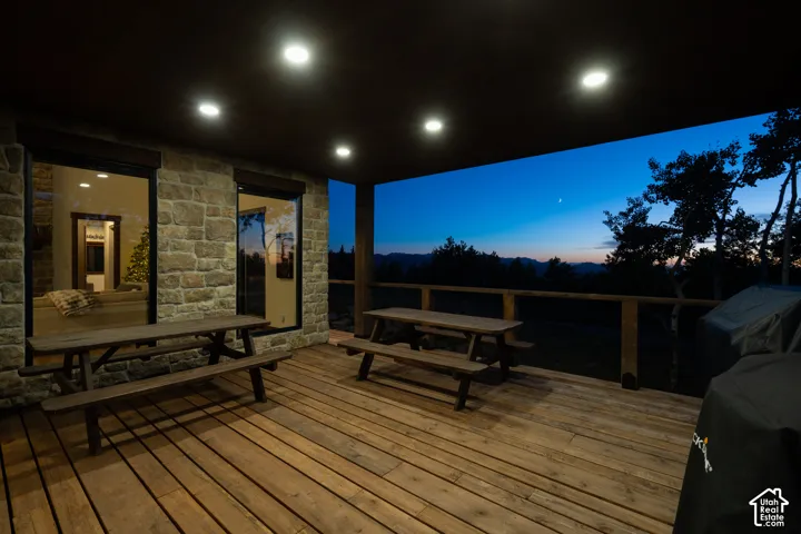 Expansive outdoor deck featuring wood flooring, stone facade, and recessed ceiling lighting
