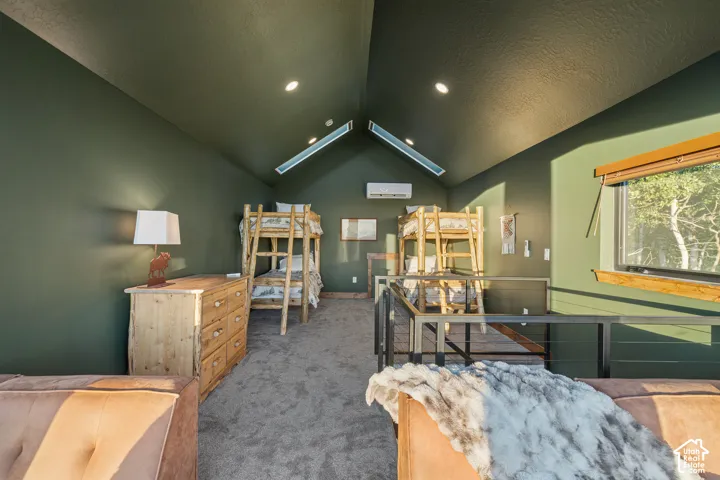 Sloped ceiling with recessed lighting and skylight, wall-mounted air conditioning unit, window with wood trim, and a metal and cable railing