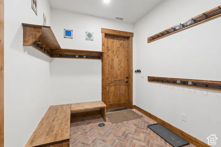 Built-in wood bench with coordinating shelving, rustic wood door, and brick-style flooring
