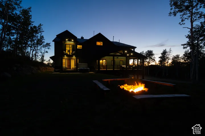 Expansive backyard featuring a built-in fire pit with surrounding wooden benches, a covered patio, and a tiered deck