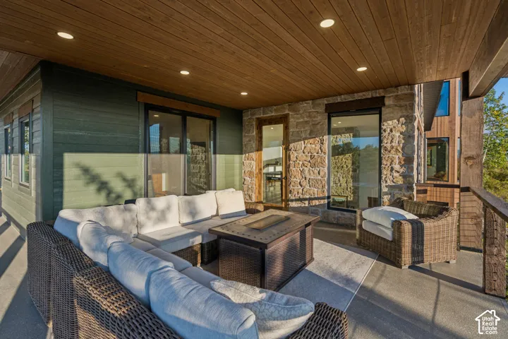 Covered outdoor terrace with recessed lighting, wood-finish ceiling, stone exterior accents, and glass railing