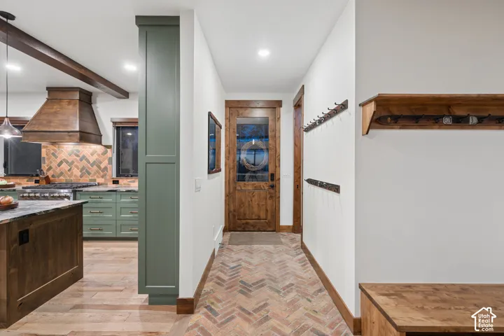 Kitchen area with green cabinetry, a wood range hood, and herringbone tile backsplash