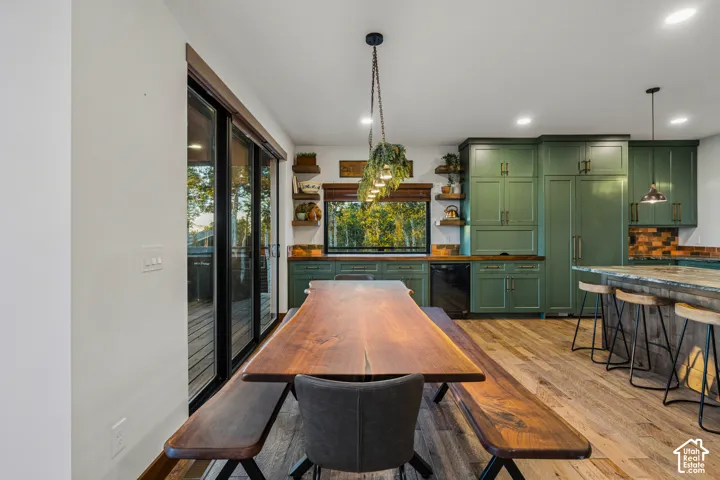 Spacious kitchen and dining area featuring rich green cabinetry, wood-finish flooring, a large island with seating, a built-in refrigerator, and expansive sliding glass doors