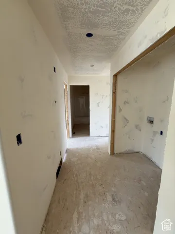Interior under construction featuring unfinished drywall, a textured ceiling, recessed lighting housing, and wood-framed entryways