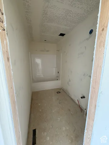 Bathroom featuring a pre-installed white acrylic tub and surround, light-toned large-format floor tile, and unfinished wall surfaces