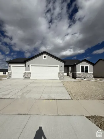 Single-story exterior featuring a concrete driveway, three-car garage, gray siding, and stone veneer accents