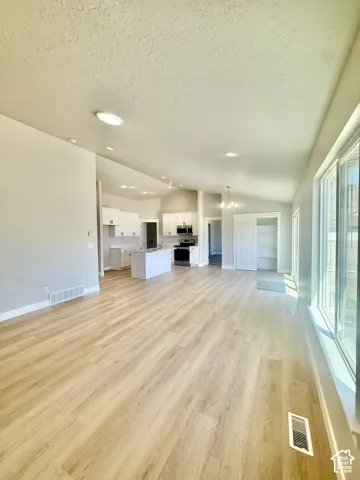 Open concept interior featuring wood-finish flooring, vaulted ceilings, white cabinetry, a center kitchen island, and a built-in pantry with a sliding door