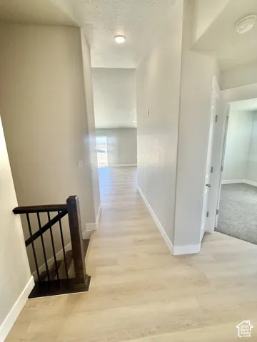Hallway featuring light wood-finish flooring, recessed lighting, and a staircase with a dark wood-finished handrail and black metal balusters