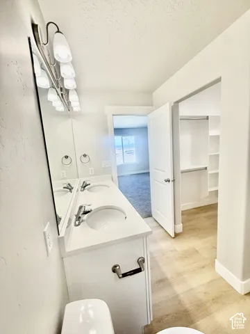 Dual-sink vanity with a solid-surface countertop, full-width vanity mirror, four-light fixture, and built-in closet storage