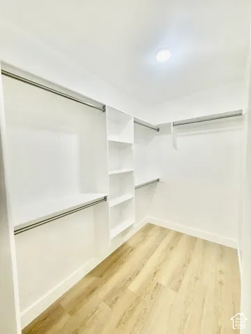 Walk-in storage space featuring wood-finish flooring, white built-in shelving, and dual-level metal hanging rods