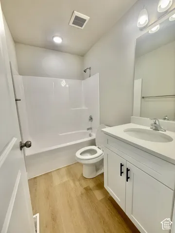 Bathroom featuring wood-finish flooring, white cabinetry with matte black hardware, stone-surface countertop, integrated vanity sink, and a white tub-shower surround