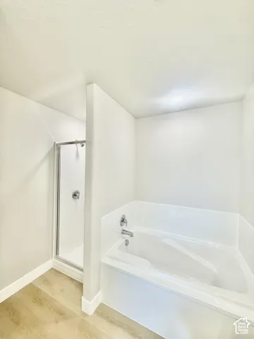 Bathroom featuring a built-in soaking tub with a surrounding surround, a glass-enclosed shower stall with metal hardware, recessed lighting, and wood-finish flooring