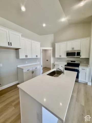 Kitchen featuring white shaker cabinetry, quartz countertops, a central island with an undermount stainless steel sink, stainless steel appliances, and wood-finish flooring
