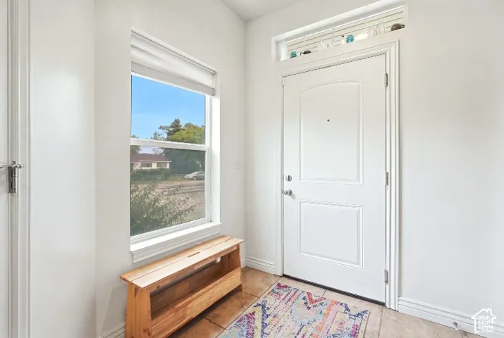 Entryway featuring a solid panel door, rectangular transom window, large picture window, and neutral tile flooring
