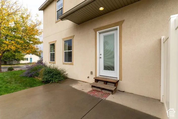 Stucco exterior featuring dual-pane windows with decorative trim, a glass-panel entry door, an overhang with recessed lighting, and a concrete patio