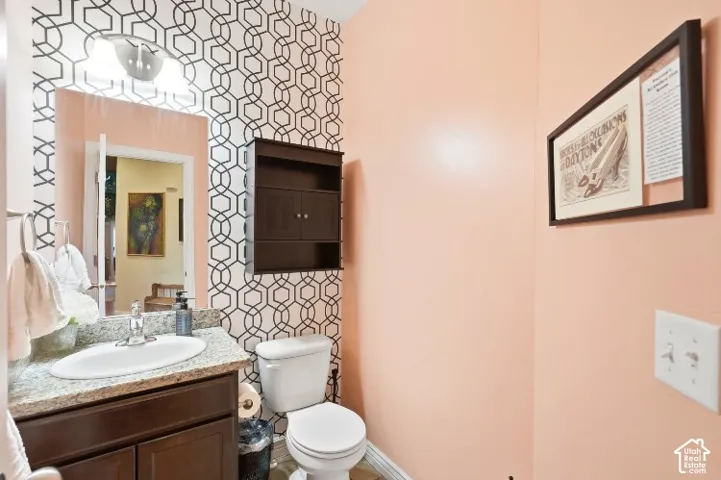 Wall-mounted dark wood cabinetry, patterned accent wall, stone-finish vanity countertop with an integrated oval basin, and chrome-finish hardware