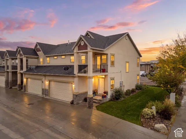 Multi-level exterior featuring stucco siding, stone veneer accents, integrated two-car garage, and covered upper-level balcony