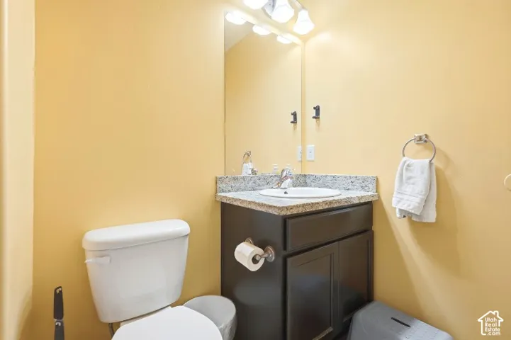Dark finish vanity cabinet with stone-look countertop, integrated sink, polished metal faucet, and wall-mounted vanity lighting