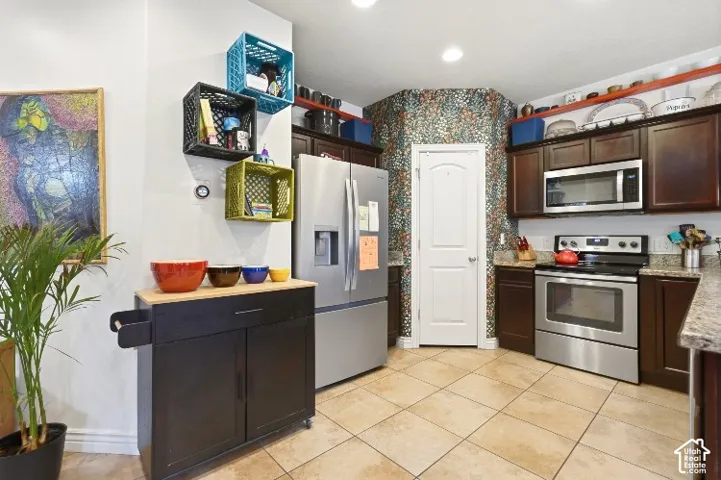 Kitchen featuring dark wood cabinetry, stainless steel appliances, stone-finish countertops, and ceramic tile flooring