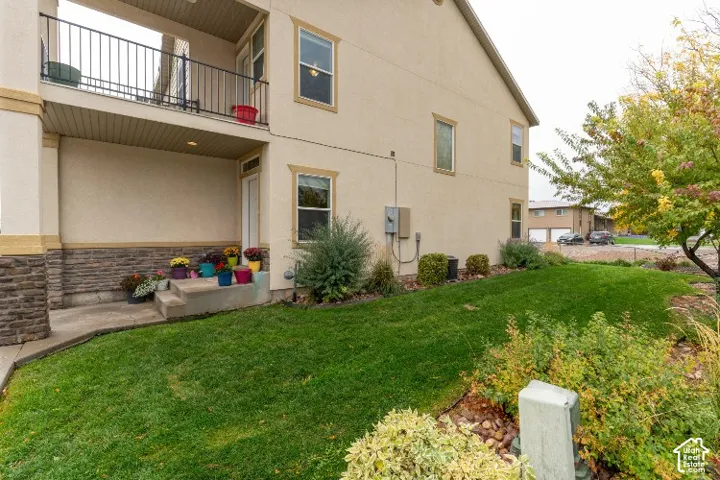 Stucco and stone veneer exterior featuring an upper-level balcony with metal railing, concrete entry steps, and a manicured lawn