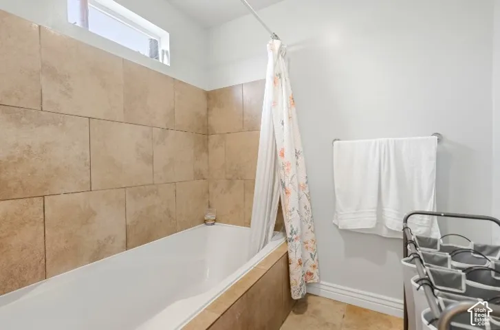 Bathtub surround featuring large-format tan ceramic tiles, integrated porcelain tub, transom window, and stone-finish flooring