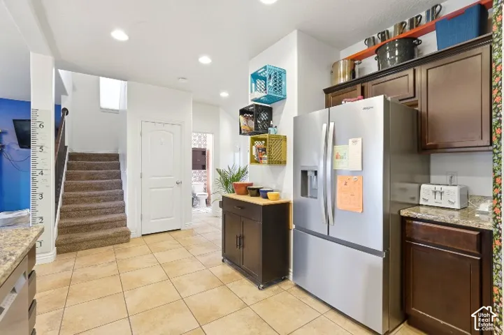 Kitchen featuring dark wood cabinetry, stainless steel refrigerator, stone-composite countertops, and tile flooring