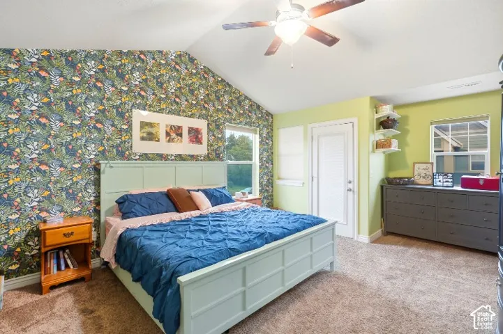 Vaulted ceilings with a central lighted ceiling fan, patterned wall covering, multiple windows, and a glass-paneled exterior door