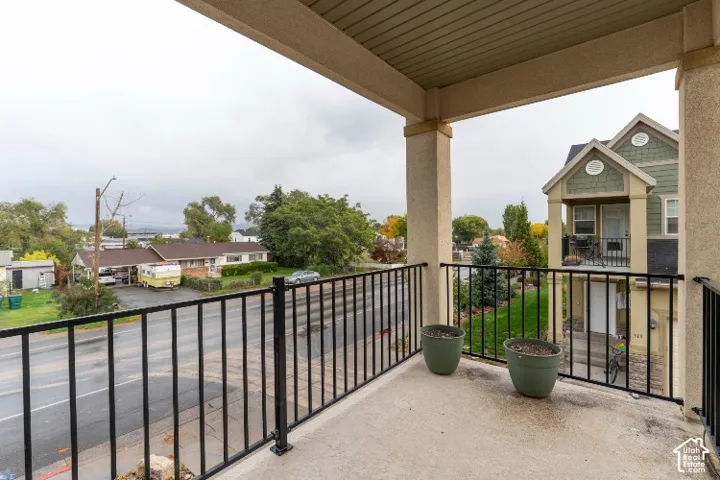 Covered balcony featuring concrete flooring, black metal railing, and structural pillars